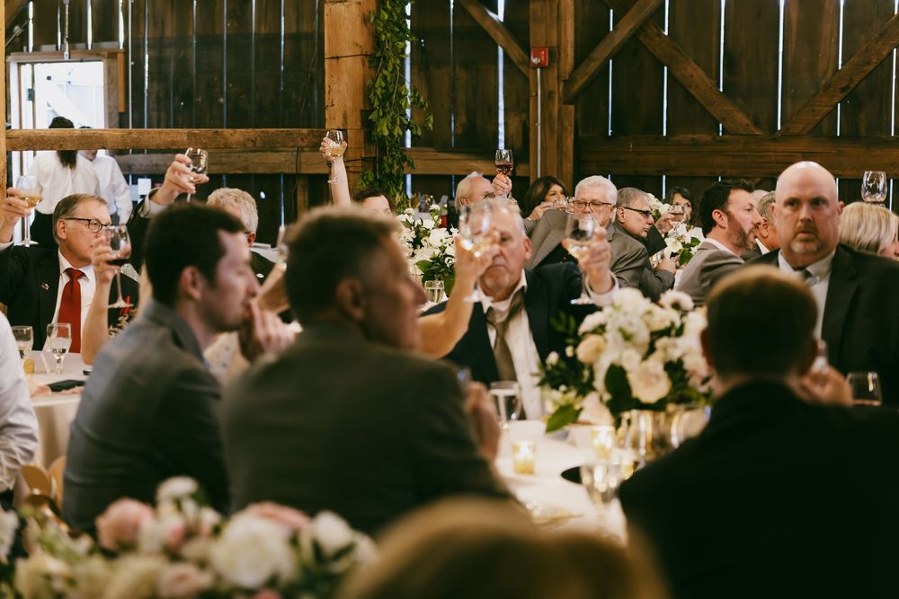 A large group of wedding guests seated at long tables in a rustic barn venue during a reception celebration.