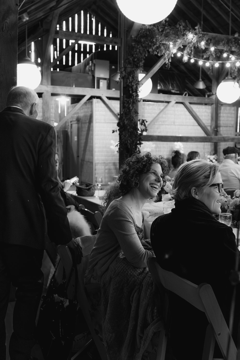 Black and white photo of guests enjoying an evening reception under string lights in a rustic barn venue.