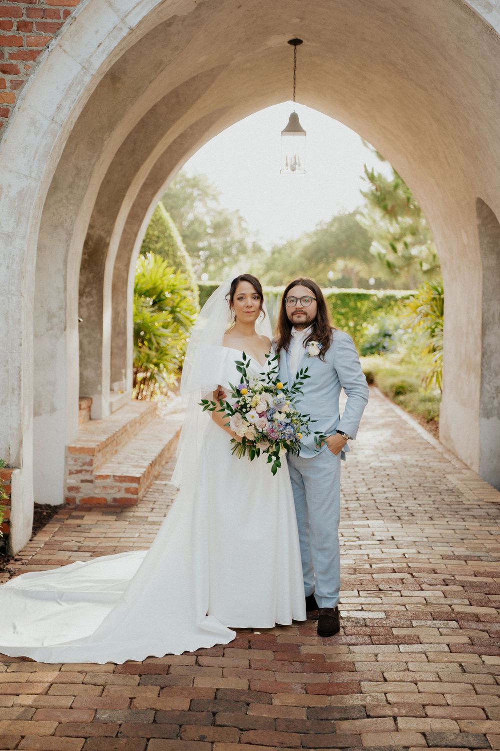 A couple poses under a series of arched brick walkways during a wedding photoshoot.