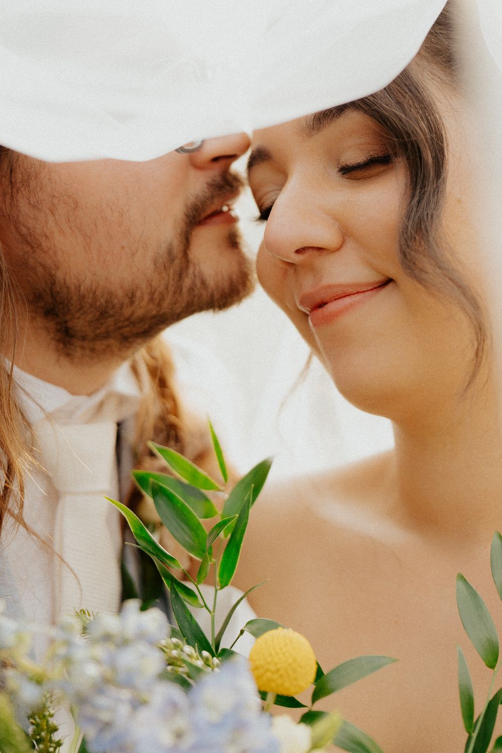 A romantic couple shares an intimate moment with yellow and green floral decorations in a soft, warm-toned setting.