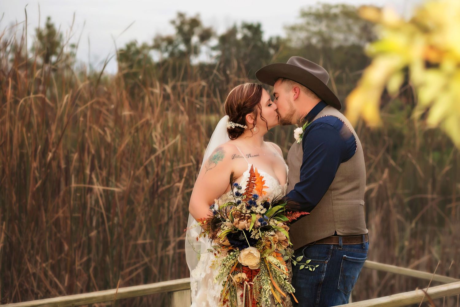 A happy couple embraces outdoors on their wedding day with a coral and peach floral bouquet in a sunlit garden setting.