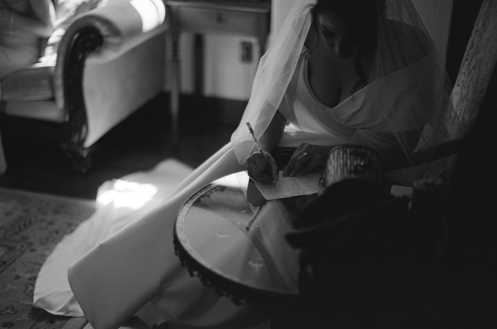 Black and white image showing hands adjusting a flowing white dress or gown in soft lighting.