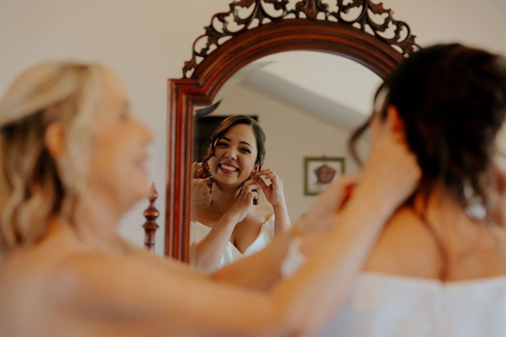 Bride getting ready in front of ornate mirror with warm lighting and vintage decor.