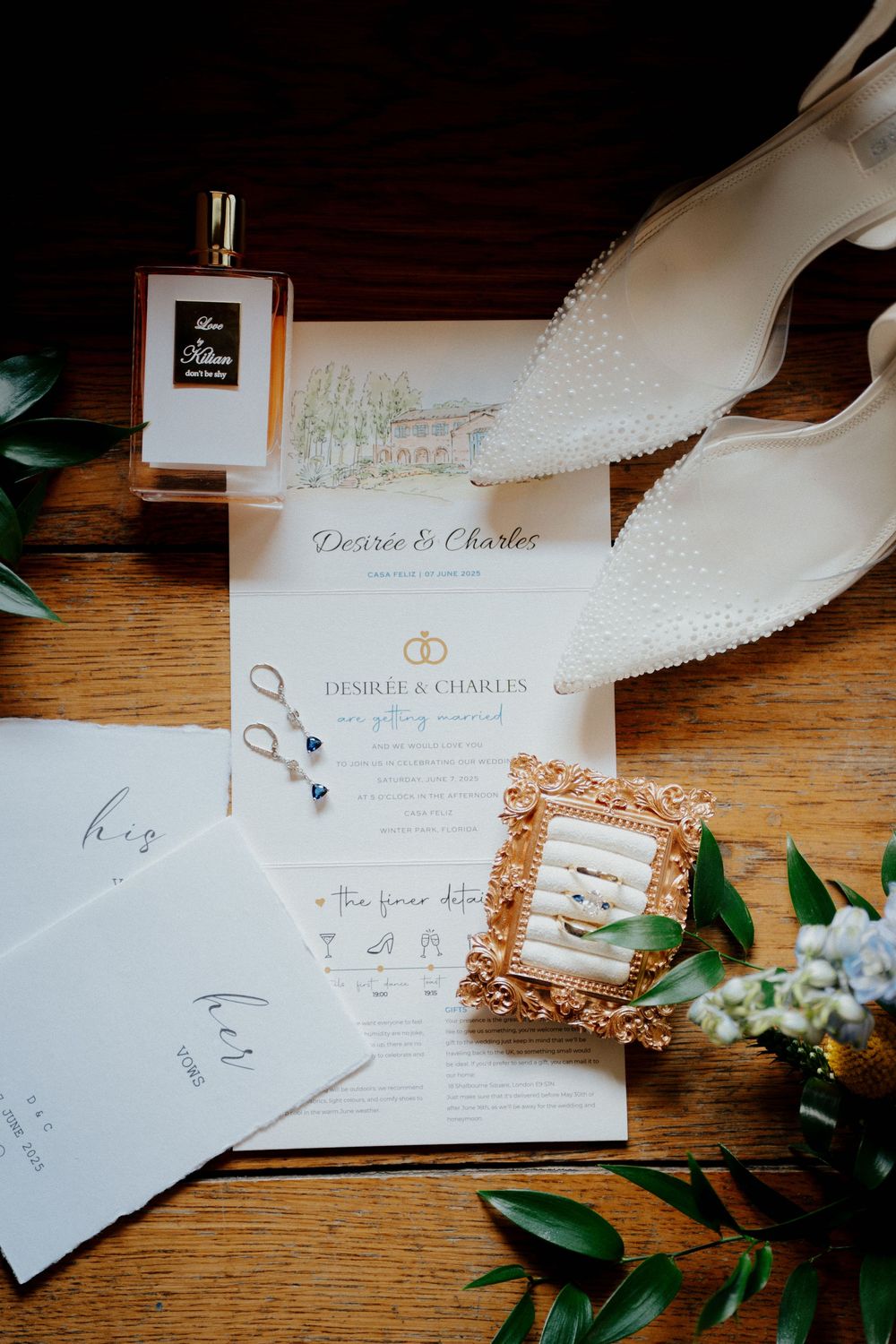 Wedding invitations and stationery with rose gold details laid out on a rustic wooden surface with greenery accents.
