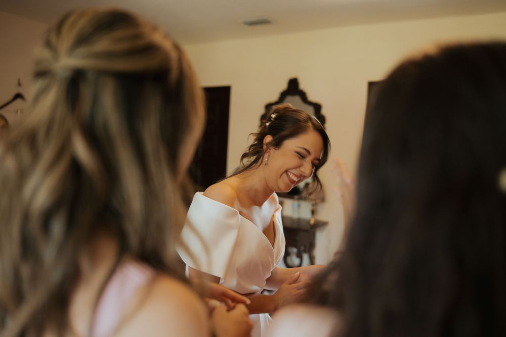 A bride getting ready on her wedding day with professional hair and makeup styling in a warm-lit room.