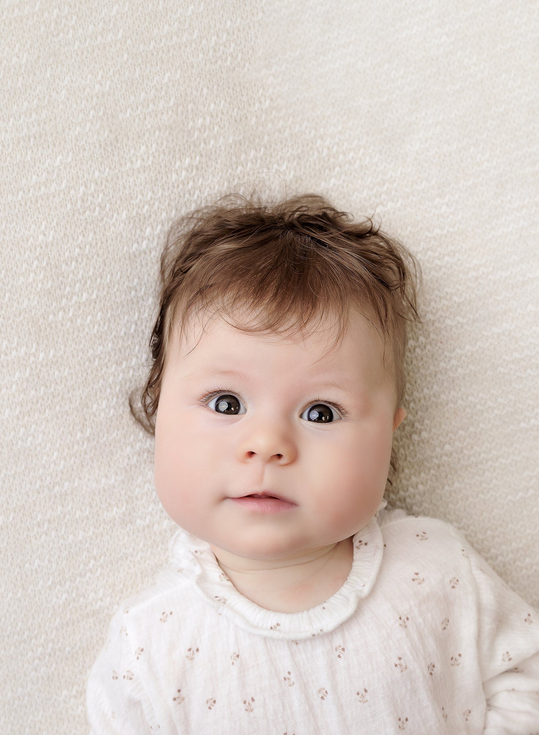 Baby plan baby approx 3 months old posed on neutral background, chubby cheeks, tossled hair looking into camera posed naturally.
