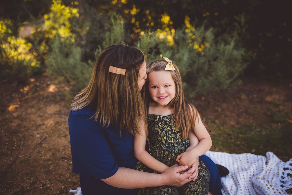 Family members sit together on a blanket in a wooded area during golden hour sunset photography session.