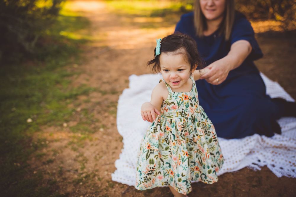Family photo session in a park during golden hour with parents and child wearing coordinated outfits on a blanket.