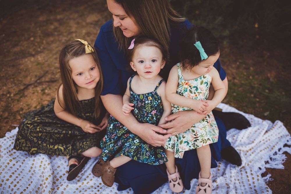Family group wearing coordinated navy and floral outfits sits together on white blanket for outdoor portrait session.