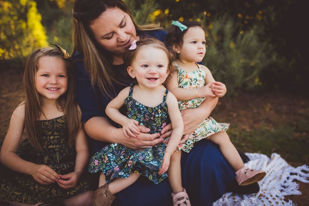 A tender outdoor family photoshoot at sunset with floral dresses and natural lighting in a garden setting.