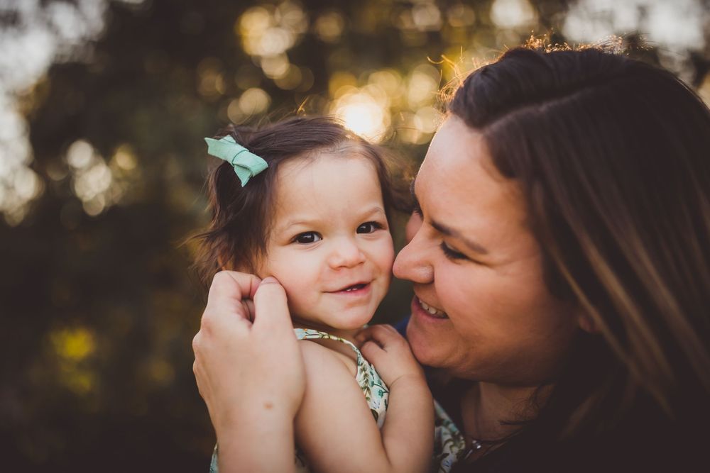 A parent and child share a tender outdoor moment in golden sunlight while playing with a small butterfly.
