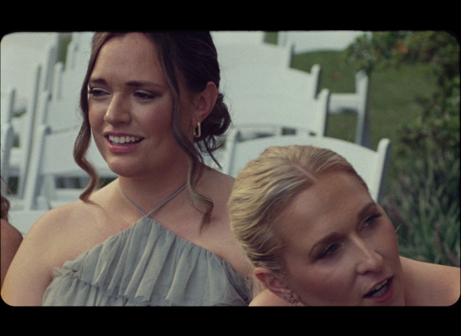 Two women in formal attire smile together at an outdoor event.