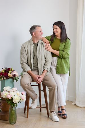 Two people share a lighthearted moment together while sitting on wooden stools in a bright minimalist setting.