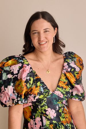 Woman wearing a vibrant floral dress with puff sleeves and a v-neckline against a neutral background.