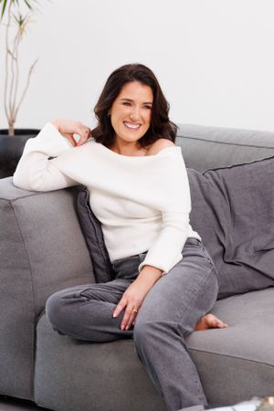 Casual lifestyle portrait on grey couch wearing white sweater and jeans. Personal Branding Photography.