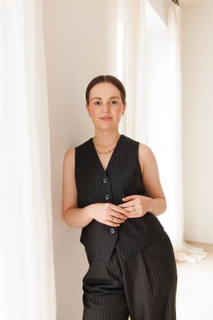 Professional portrait in black pinstripe sleeveless outfit against white curtains. Personal Branding Photography.