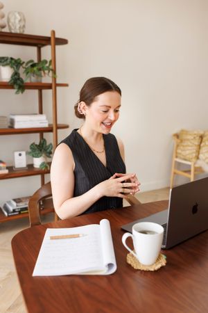 Professional business owner working on laptop at wooden desk with coffee and papers in cozy home office setting.Personal Branding Photograpy