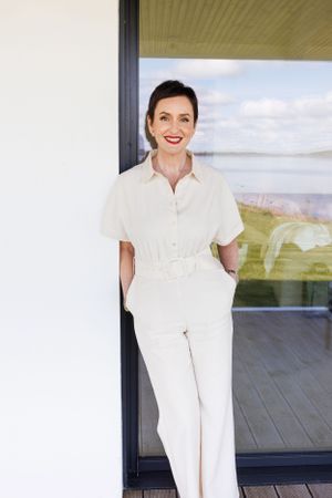 Stylish person in all-white outfit standing in doorway with water view behind. Personal Branding Photography.