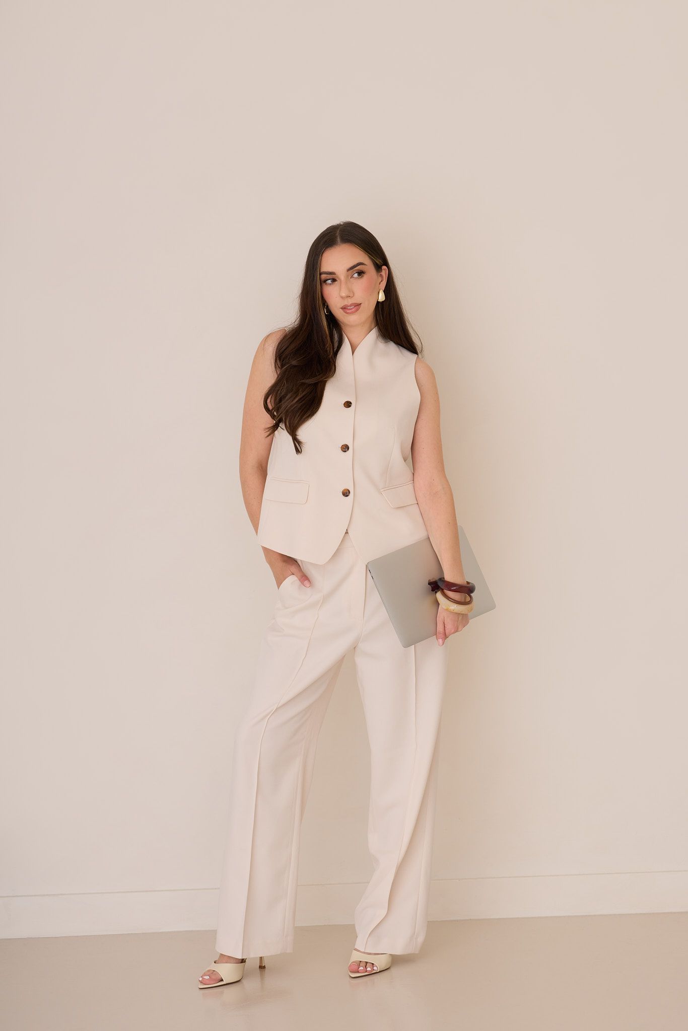 Model in all-white ensemble poses elegantly against neutral backdrop in fashion photography series.
