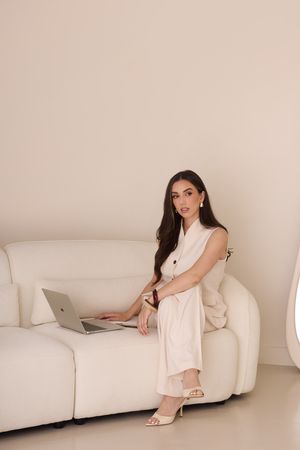 Woman in light pink loungewear relaxes on white couch in minimalist studio setting.