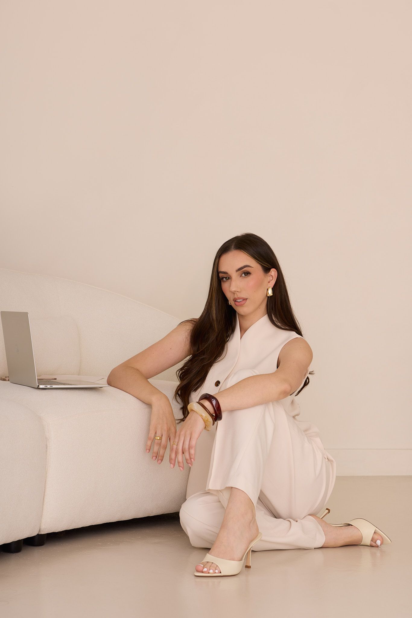 A person in a white outfit lounges on a light-colored floor with a laptop nearby.