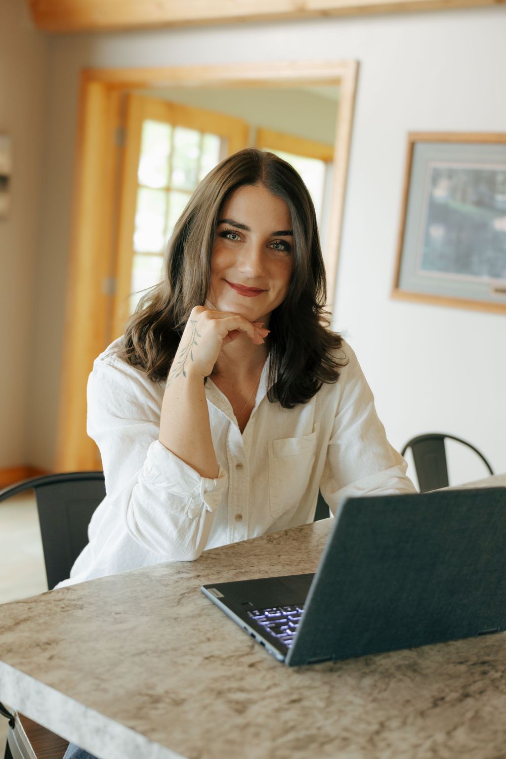 A person in a white shirt works on a laptop at a marble table in a bright, sunlit room.