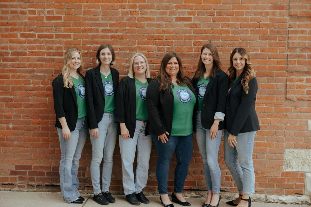 A group of people in casual attire lean against a red brick wall while posing together.