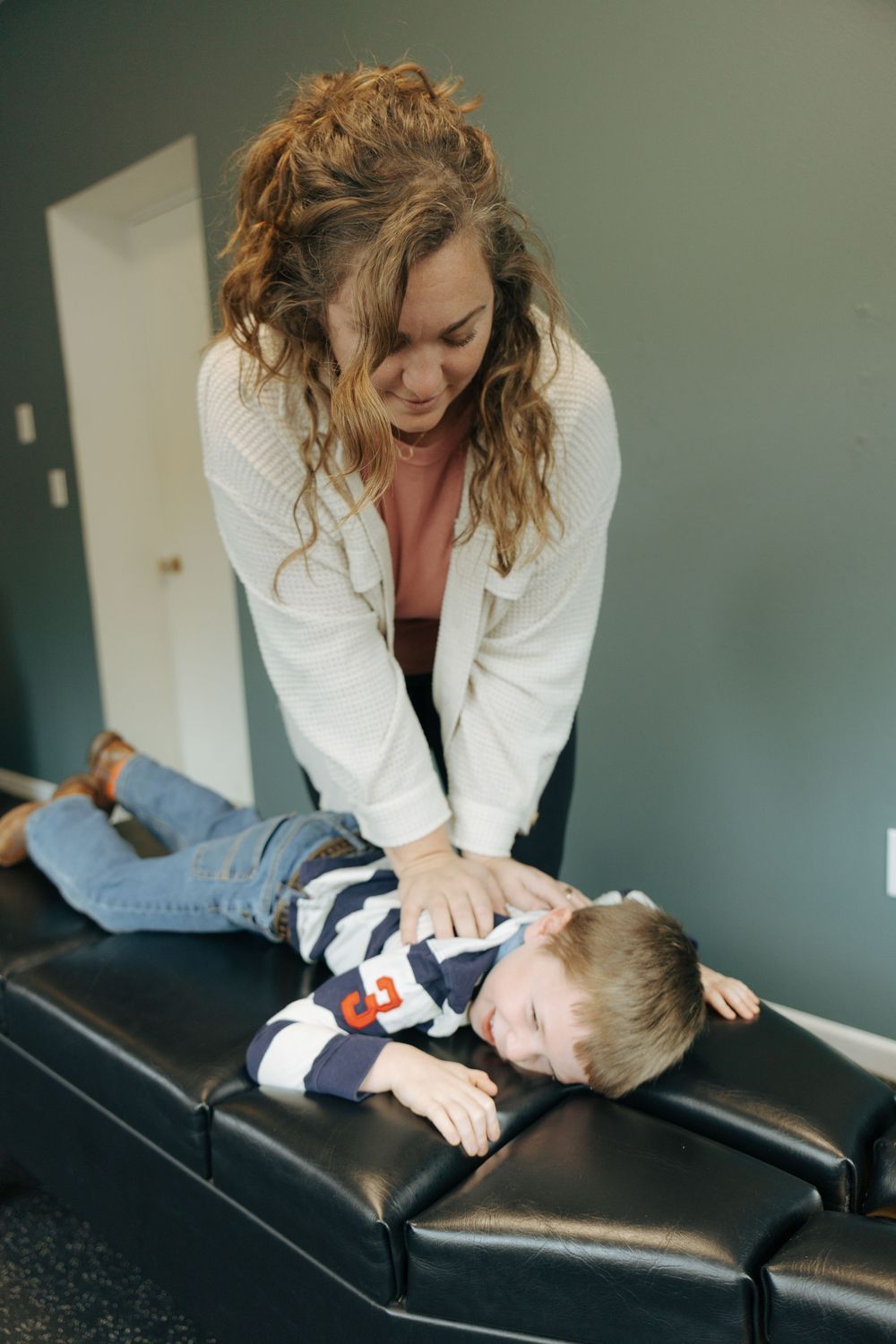 A chiropractor performs a gentle adjustment on a young patient lying on a black treatment table.