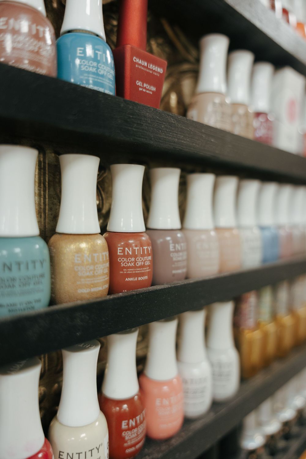 Rows of colorful nail polish bottles arranged on dark shelves in a salon or beauty store display.