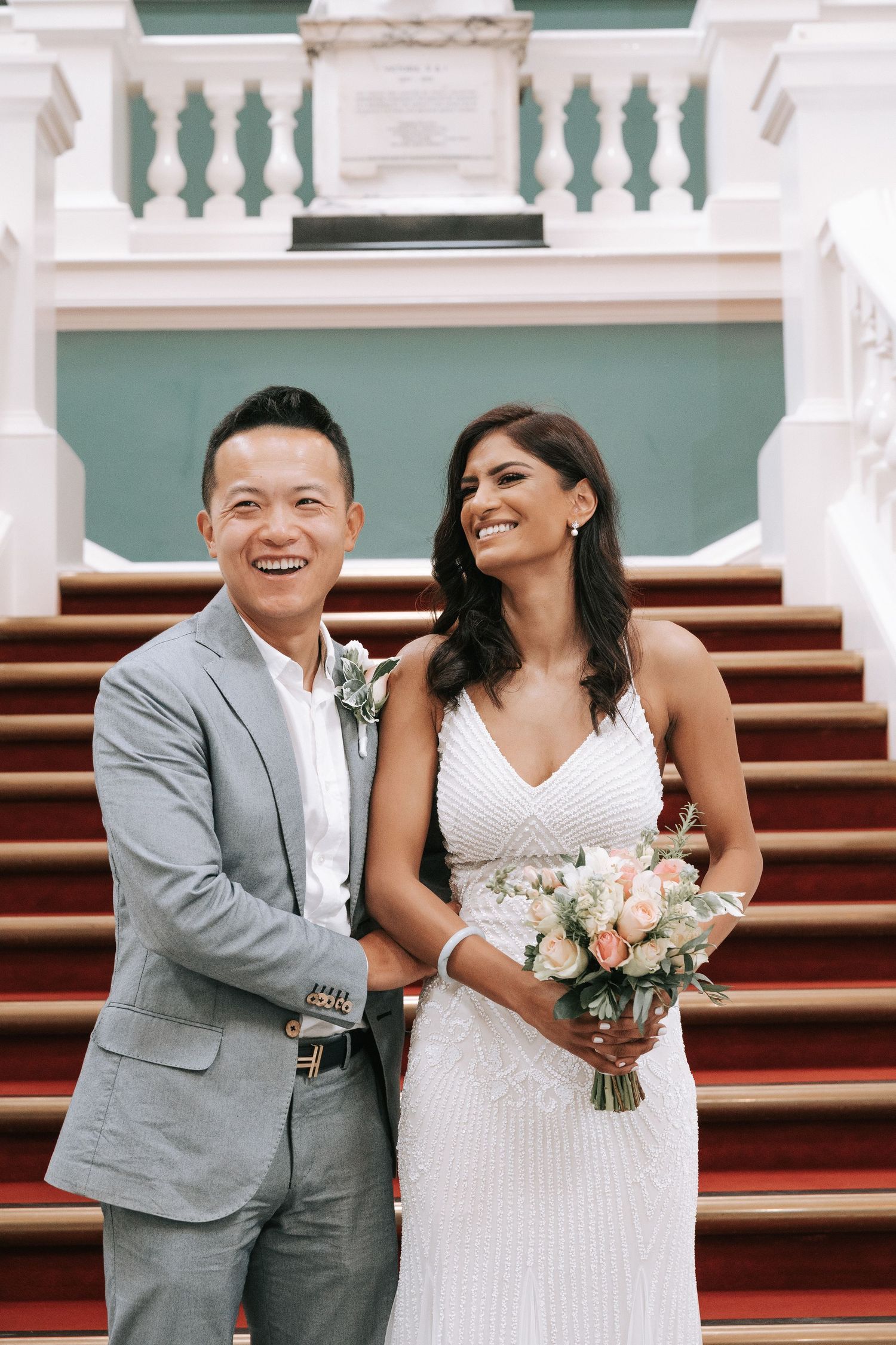 A happy couple shares joyful moments on their wedding day while standing on elegant stone steps.