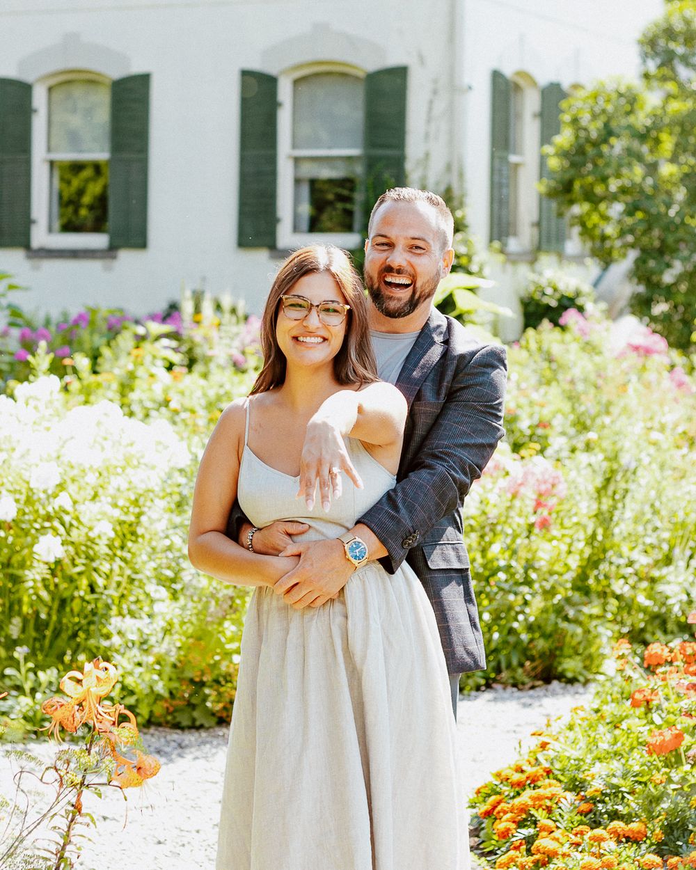 A couple embraces and laughs together in a sunny garden filled with colorful flowers.
