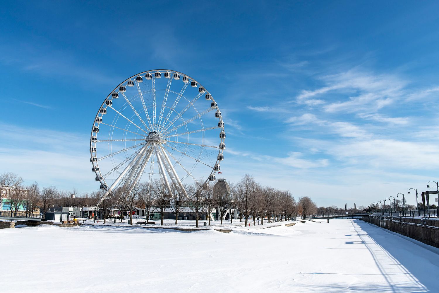A large Ferris wheel stands against a bright blue sky on a snowy winter day at Montreal's Old Port. Montreal, Canada.