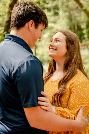 Happy couple embracing while wearing coordinating navy and yellow outfits in a forest setting.