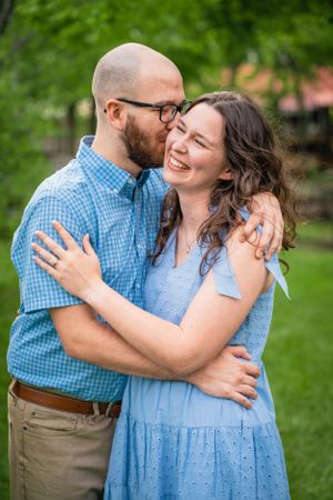 A couple shares a joyful moment embracing in a garden wearing coordinating blue outfits.