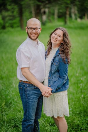 A couple poses together outdoors holding hands and smiling in casual spring attire.