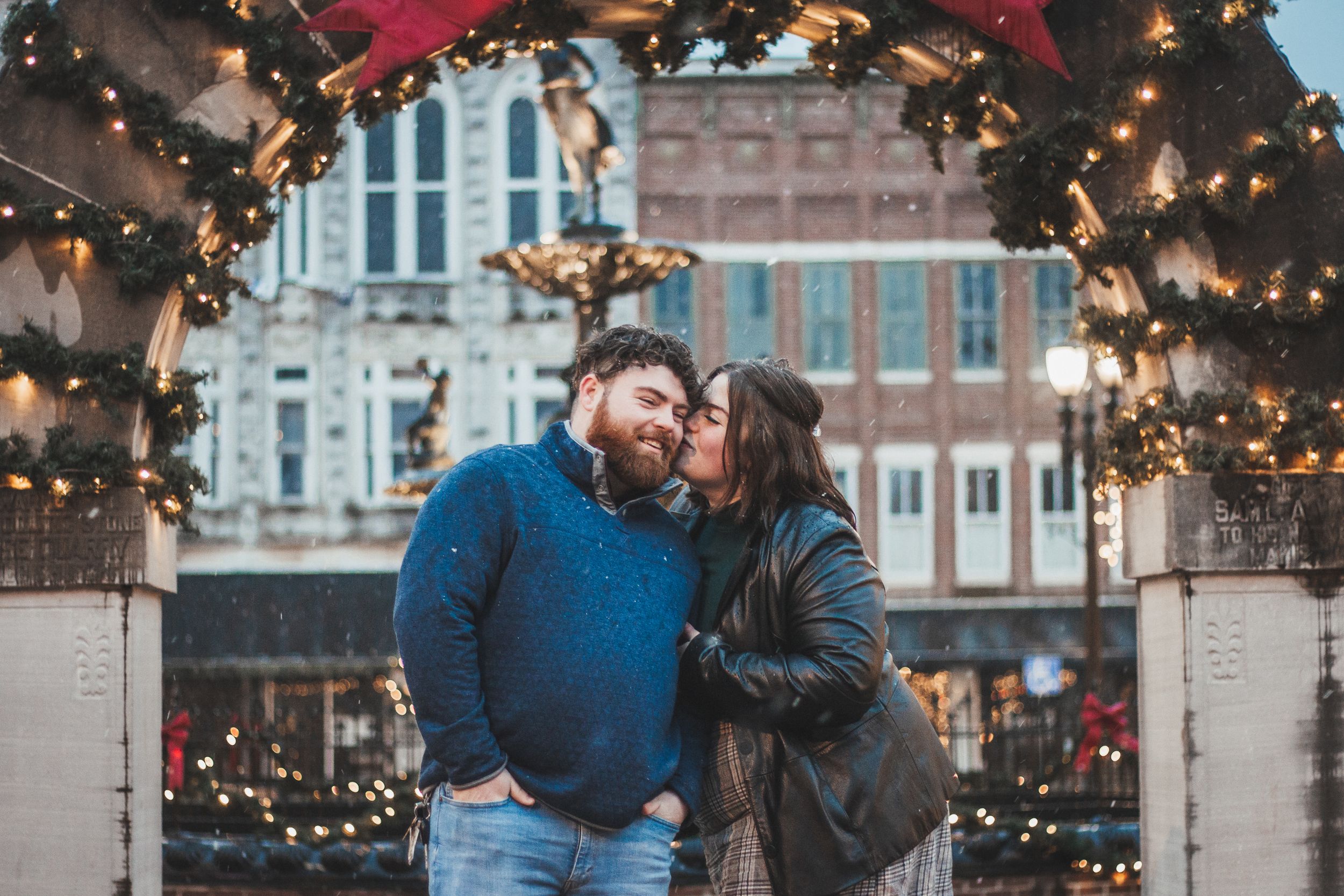 A couple shares an intimate moment under a decorated archway with twinkling holiday lights.