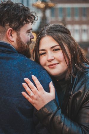 A close-up engagement photo showing a sparkling ring as a couple embraces outdoors.