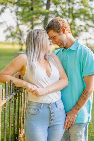Romantic couple sharing an intimate moment against a rustic fence in a sunny garden setting.