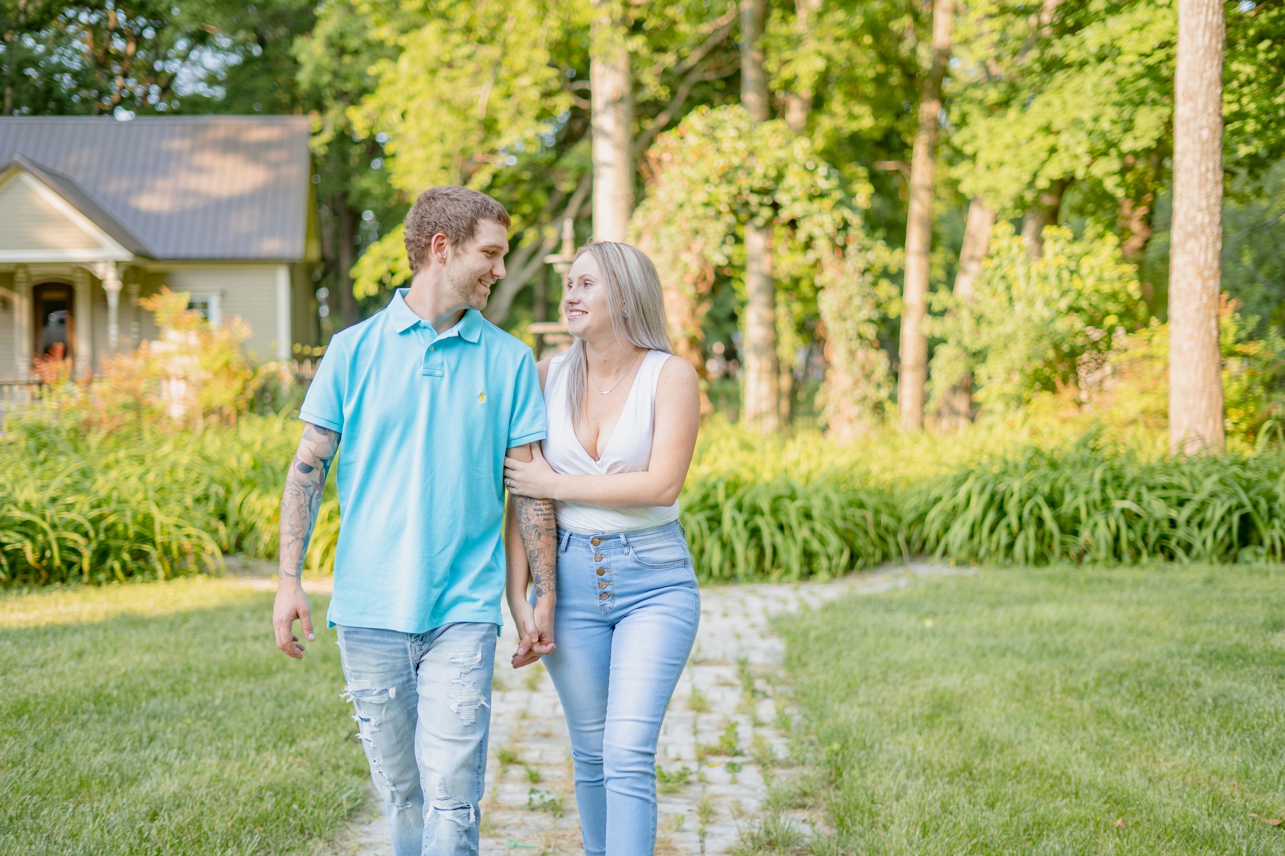 Couple walking together on lush green lawn with house and trees in background.