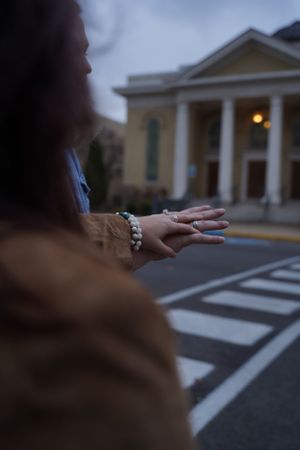 A close-up view of hands with jewelry against a building with columns at dusk.