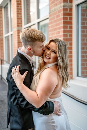 Affectionate couple embracing in indoor setting with brick wall background.