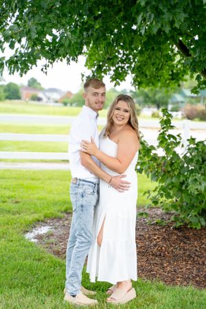 Couple embracing under green tree canopy in summer garden setting.