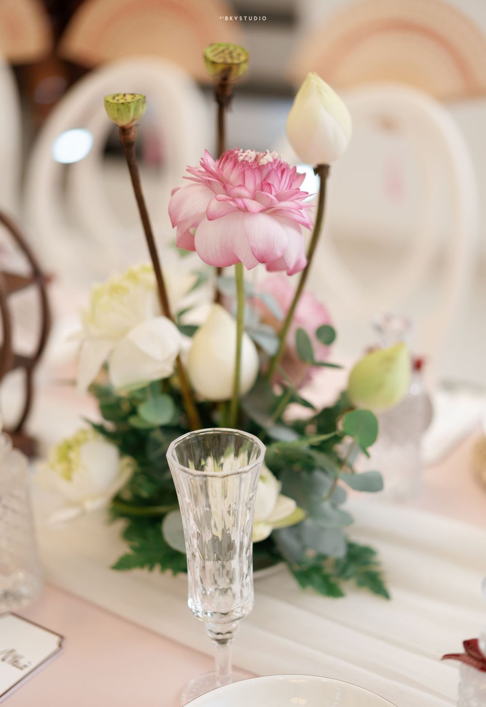 Delicate floral centerpiece with pink carnations and white roses next to crystal champagne glass.