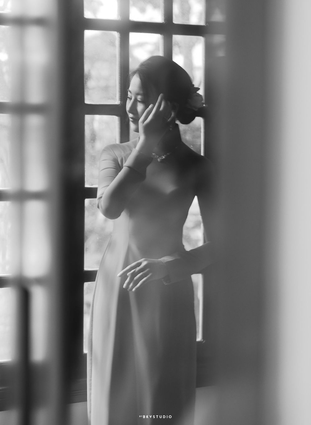 Artistic black and white portrait through a window showing a silhouette of a figure in an elegant dress.