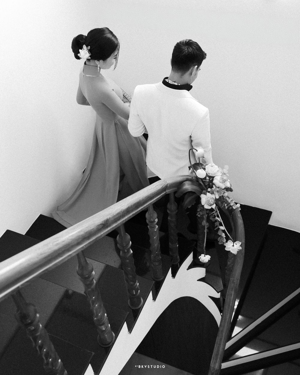 Black and white photo of a couple on elegant spiral staircase decorated with flowers.