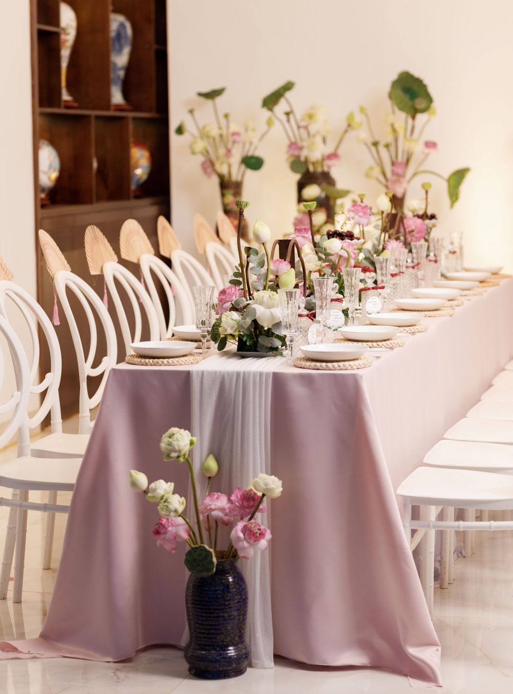 Elegant wedding table setting with pink tablecloth and white chairs decorated with delicate floral centerpieces.