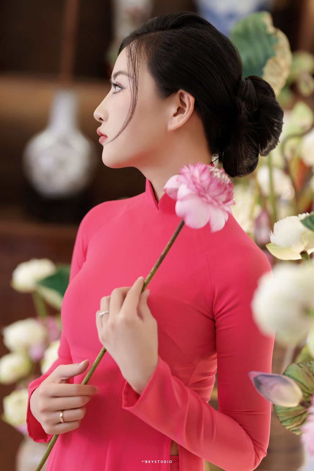 Traditional red ao dai dress adorned with pink and white flowers in an elegant interior setting.