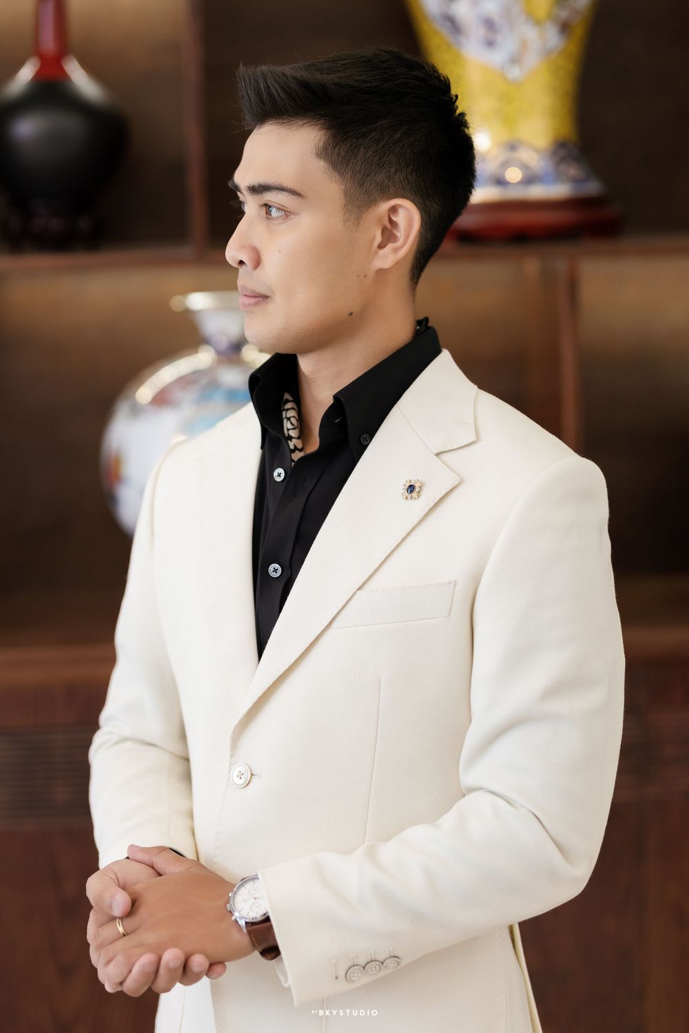 Sophisticated profile shot of person in crisp white blazer and black shirt against wooden decor.