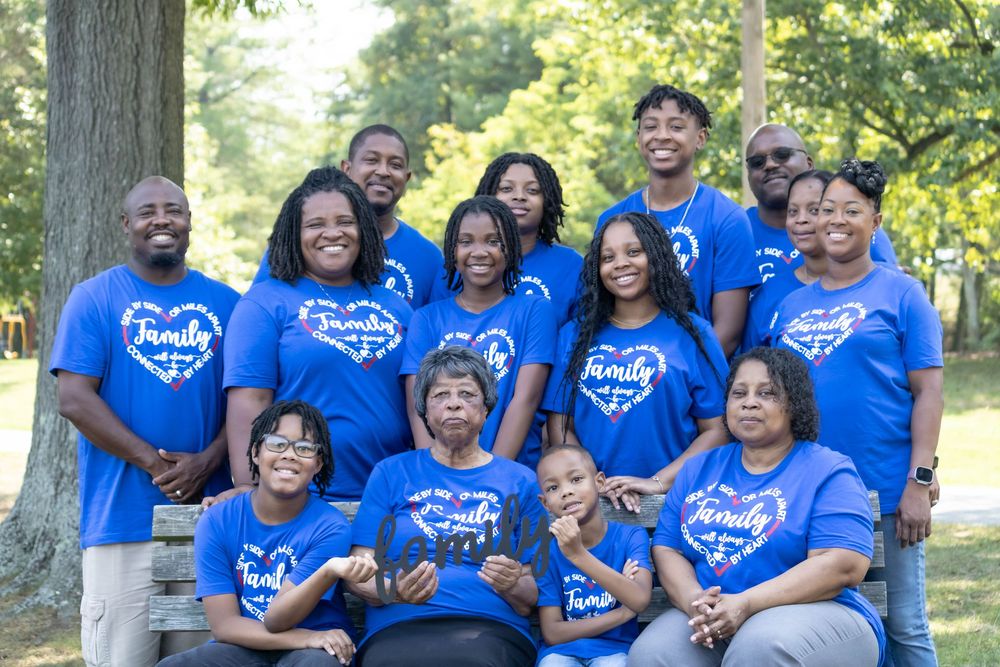 Group wearing matching bright blue t-shirts with heart designs poses together outdoors in a park setting.