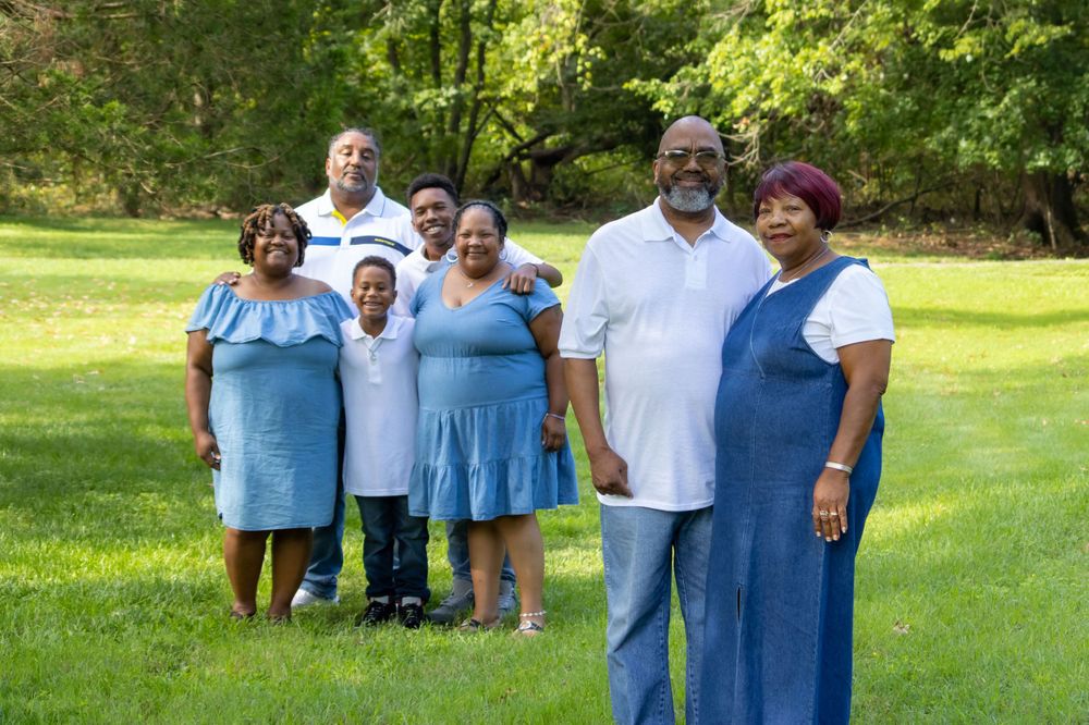 A family group poses together for a portrait in a sunny park setting.